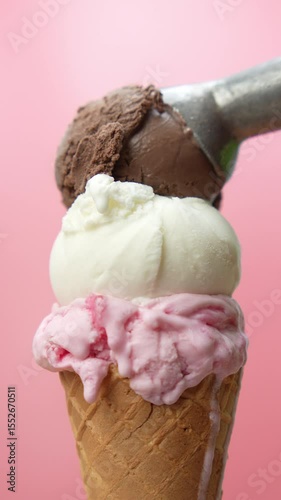 4K footage vertical video close-up Triple Scoop Ice Cream Cone with chocolate vanilla and strawberry flavors being freshly served set against a soft pink background. 