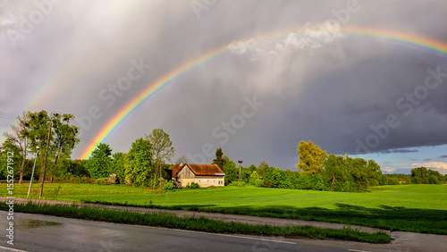 a village house in Masuria and behind it a very impressive rainbow