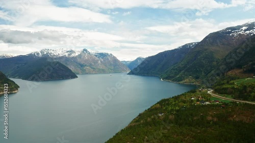 Hardanger fjord with expansive mirror waters winding through towering mountains. Peaks with patches of snow highlight rugged natural beauty of Norway