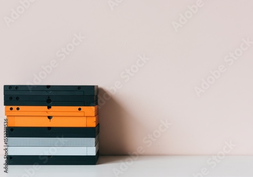 A stack of vintage videotapes sits on a white surface against a pale pink wall