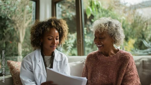 Young black woman doctor consulting elderly patient in bright living room  