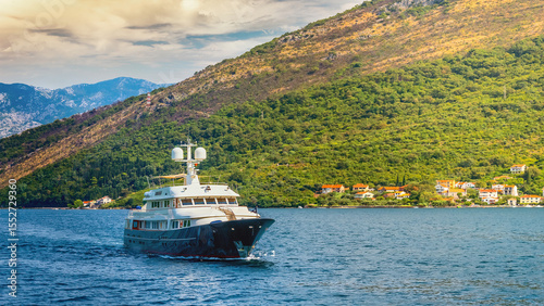 Luxury superyacht cruising on the serene blue waters of the stunning Bay of Kotor in Montenegro, with a picturesque backdrop of lush green mountains and a charming coastal village