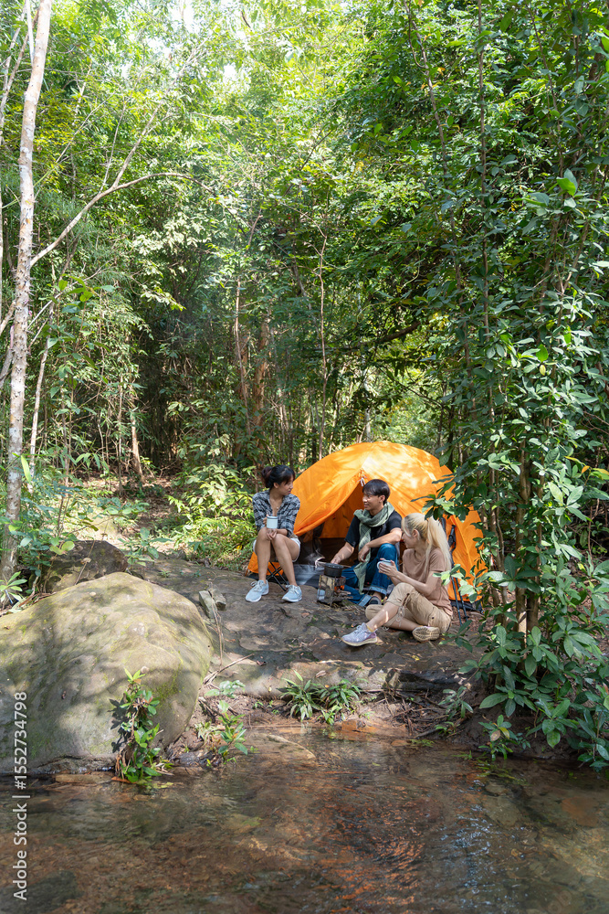 Three people are sitting in a tent in the woods. One of them is a woman. The tent is orange Three people are sitting in a tent in the woods. One of them is a woman. The tent is orange