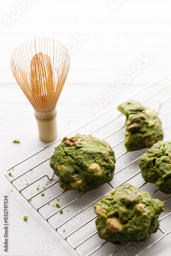 Closeup of fresh baked matcha cookies with Chasen, bamboo whisk, on white wooden background.
