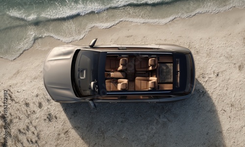 Overhead view of a light-beige SUV parked on a sandy beach near gentle waves, showcasing its panoramic sunroof and tan leather interior