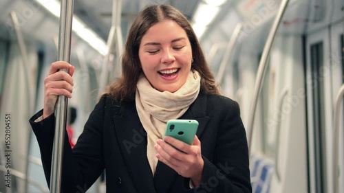 Focused female passenger holding onto a pole while using her smartphone to browse the internet and engaging with a mobile application in a subway train during her daily routine as a commuter
