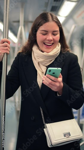 Focused female passenger holding onto a pole while using her smartphone to browse the internet and engaging with a mobile application in a subway train during her daily routine as a commuter