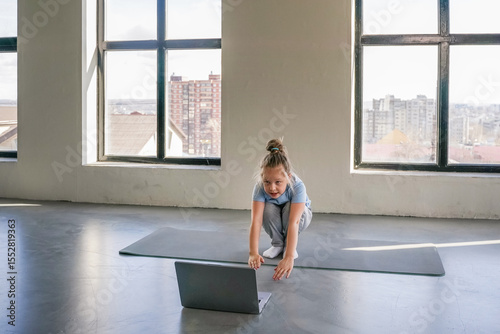 Young girl practicing yoga at home while following an online lesson during the morning hours.