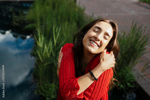 Smiling woman embracing herself in a park