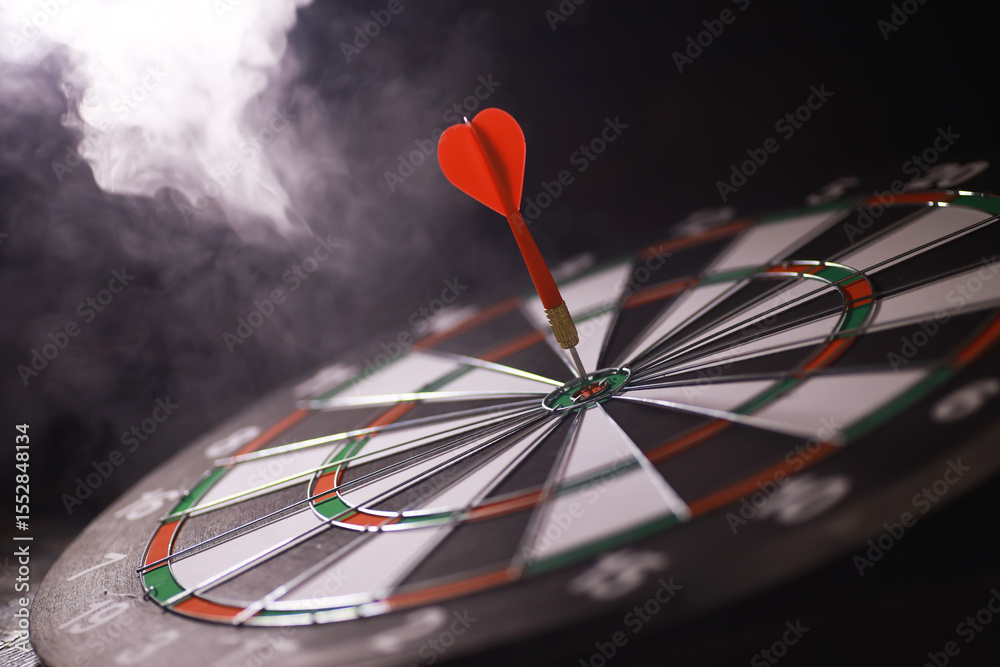 Obraz premium Bullseye Dartboard with Red Dart in Smokey Background - Precision Success Concept