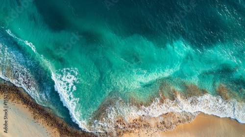 Aerial wave crashing against golden beach, green and white foam. 