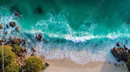 Aerial wave crashing against golden beach, green and white foam. 