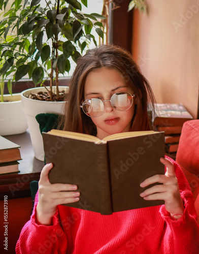 The girl is reading a book while sitting on the sofa.
