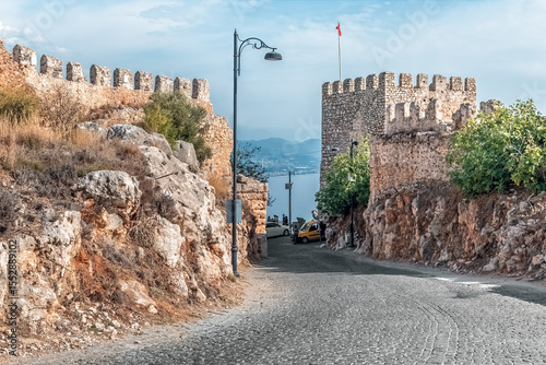 Ancient stone walls and watchtower at Alanya Castle overlooking the sea and coastal town. The historic site highlights medieval architecture and scenic views. Alanya, Turkey - October 24, 2020