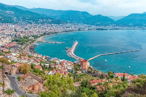 Aerial view of Alanya harbor and Red Tower with the vibrant city nestled between mountains and the Mediterranean Sea, Turkey. Serene turquoise waters surround this historic coastal town