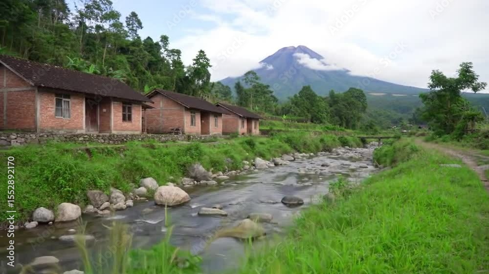 Peaceful rural village landscape with shallow river, brick houses, dirt path, lush greenery, and volcano peak beneath blue cloudy sky Peaceful rural village landscape with shallow river, brick houses, dirt path, lush greenery, and volcano peak beneath blue cloudy sky