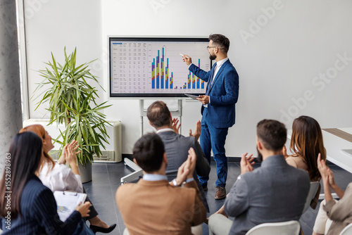 Billede på lærred Financial analyst is standing at conference room and presenting statistics with charts and numbers on interactive board in front of audience who is applauding