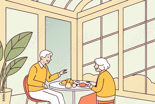 A joyful Caucasian senior couple dines, with the man in a yellow sweater engaging in conversation over a bright breakfast spread in a sunlit hotel conservatory.