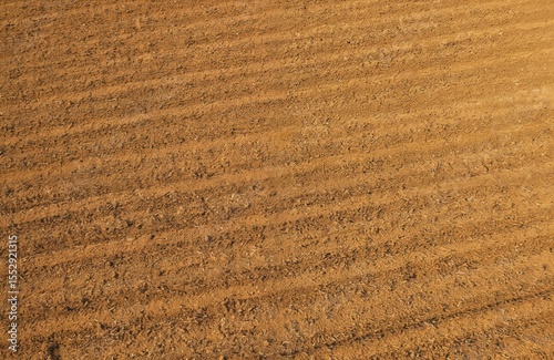 Top view of brown ploughed cassava land soil with line pattern after harvesting. Soil texture tilled agricultural ground. Earth prepared for new crop planting, cultivation. Field preparation,