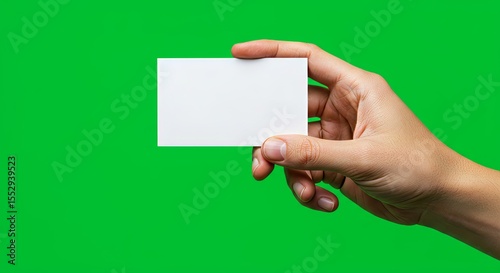 Hand holding blank white card against vibrant green background, studio shot