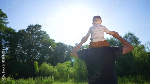Man holding child in field. Father and child are outdoors with their father and son. A tree in the sunshine and green bonding nature. A man with a child in a field lifestyle.