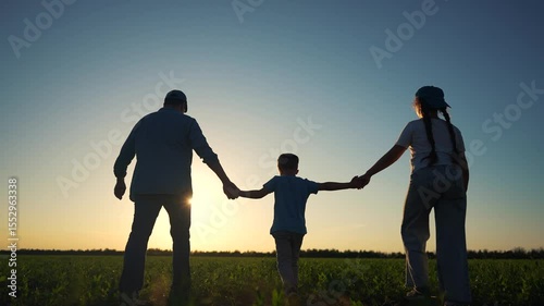Silhouette of family walking in a field at sunset. Family walking in a field at sunset. Silhouette of parents and child outdoors. The outline of a family strolling through a meadow during lifestyle.