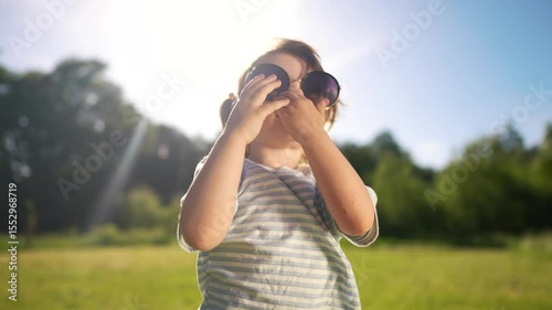 Child wearing sunglasses in the sun. A young girl in sunglasses and sunlight outdoors. A young girl is playing in a field of bright sunshine and nature. Kid sporting sunglasses under the lifestyle.