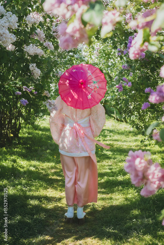 Dreamy portrait of a mysterious geisha-cosplay inspired beauty. Porcelain-skinned woman in a pink ornate Chinese silk robe (Hanfu), short black hair, posing gracefully with Asian parasol on the bloomi