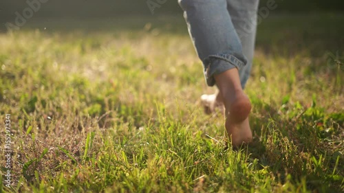 Person walking through field. A child is walking outdoors with bare feet. A pair of jeans and a t-shirt with sunlight relaxing in the summer. An individual strolling through a meadow lifestyle.