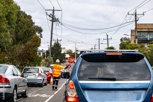 Traffic controller directing vehicles with a stop sign during roadwork on a suburban Australian street. Cars are queued as part of temporary traffic management near a construction zone in Melbourne.