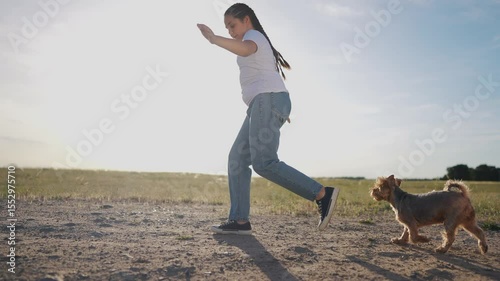 Woman walking her dog in field. Girl is walking dog outside in the summer. Pair of casual jeans with a playful nature in the grass. A woman taking her dog for a walk in a field lifestyle.
