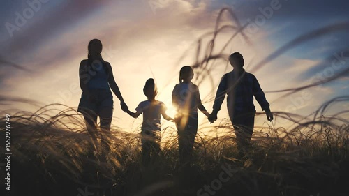Family walking in field at sunset. Silhouette of parents and family walking at sunset. A child holding hands with a mother outside. A family strolls through a field lifestyle during sunset.