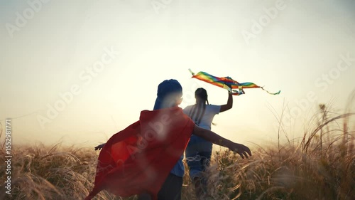 Two children in field with kite. Children running in field with kite. Playful adventure with a sunset and imagination. A pair of kids in a meadow flying a lifestyle kite.