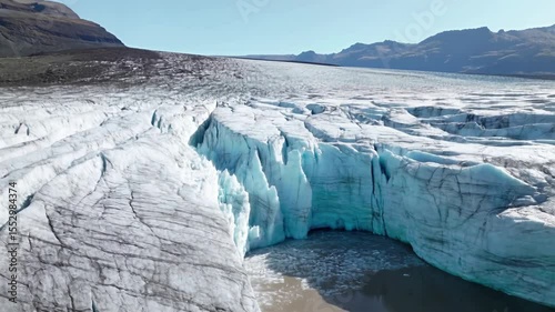 Expansive Aerial View of Melting Glacier Flowing into Serene Lake Beneath Bright Blue Sky