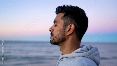 Profile view of a man, eyes closed, with a thoughtful expression,  against a pastel sky and blurred ocean