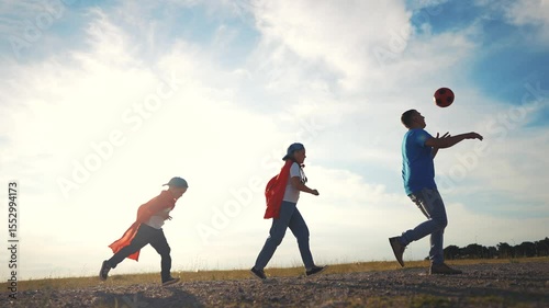 Family playing football. Father and children playing football outdoors. A young girl running in the sunny sky with her capes. Family playing soccer lifestyle.
