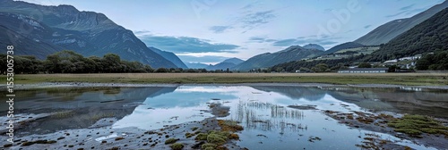 Vue panoramique d'un lac ou d'un marécage reflétant des montagnes sombres et un ciel bleu-gris nuageux, avec de l'herbe