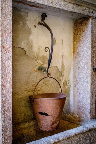 Historical stone fountain against a rustic wall in an Italian village, showcasing intricate craftsmanship and timeless charm in a serene setting