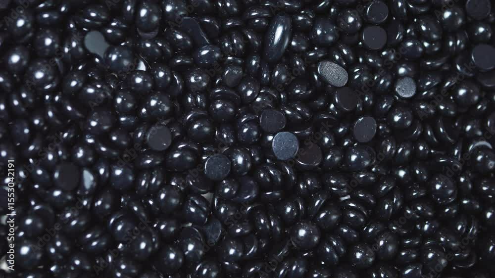 Glossy black hard wax beans covering entire frame, displaying irregular shapes with smooth, reflective surface for professional hair removal process