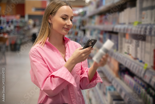 Woman scanning product barcodes with a smartphone while shopping for cosmetics in a supermarket, checking detailed information and comparing prices before making a purchase