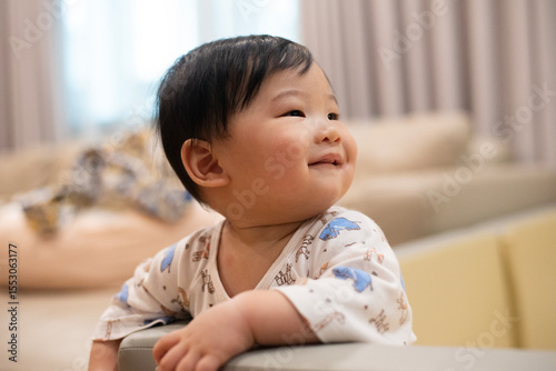 A little asian child baby proud for climb and hold onto playpen wall with his smile. He practice to standing and walking. Development Baby aged of 8 months concept.