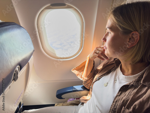 Passenger woman is flying in plane. Girl sitting in airplane looking out window going on trip vacation travel. Traveling female inside plane enjoying flight. Traveling girl