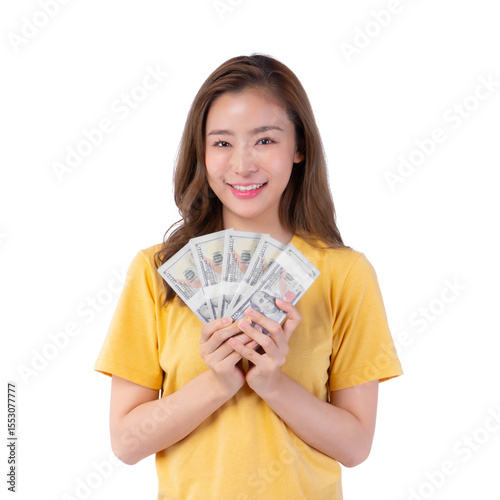 Happy young Asian woman in yellow t-shirt smiling and holding fan of US dollar bills in hands, isolated on a transparent background, concept of success, finance, earnings and wealth