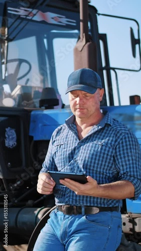 Farmer is using digital tablet. on farm field, near tractor, on farm machinery backdrop. smart farming. farming technologies