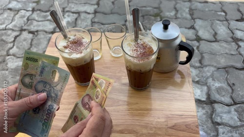 Man count Vietnamese dong banknotes above coffee on wooden table in outdoor cafe