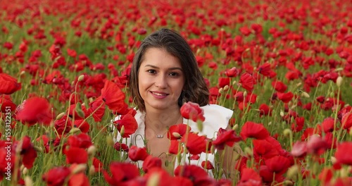 Young woman in a white dress posing among summer poppies