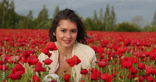 Young woman in a white dress posing among summer poppies