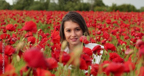 Young woman in a white dress posing among summer poppies