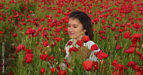 Young woman in a white dress posing among summer poppies