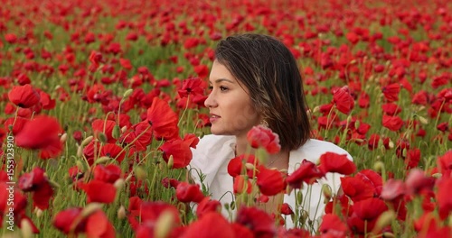 Young woman in a white dress posing among summer poppies